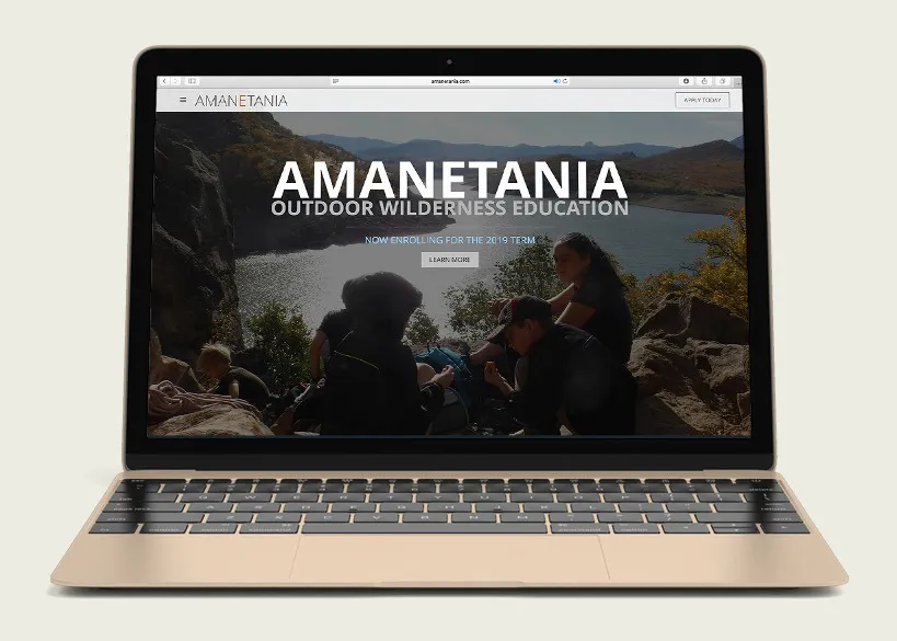 The Amanetania website home on a laptop: participants sitting on a rock ledge above a lake, with the Amanetania name and the line Outdoor Wilderness Education across it