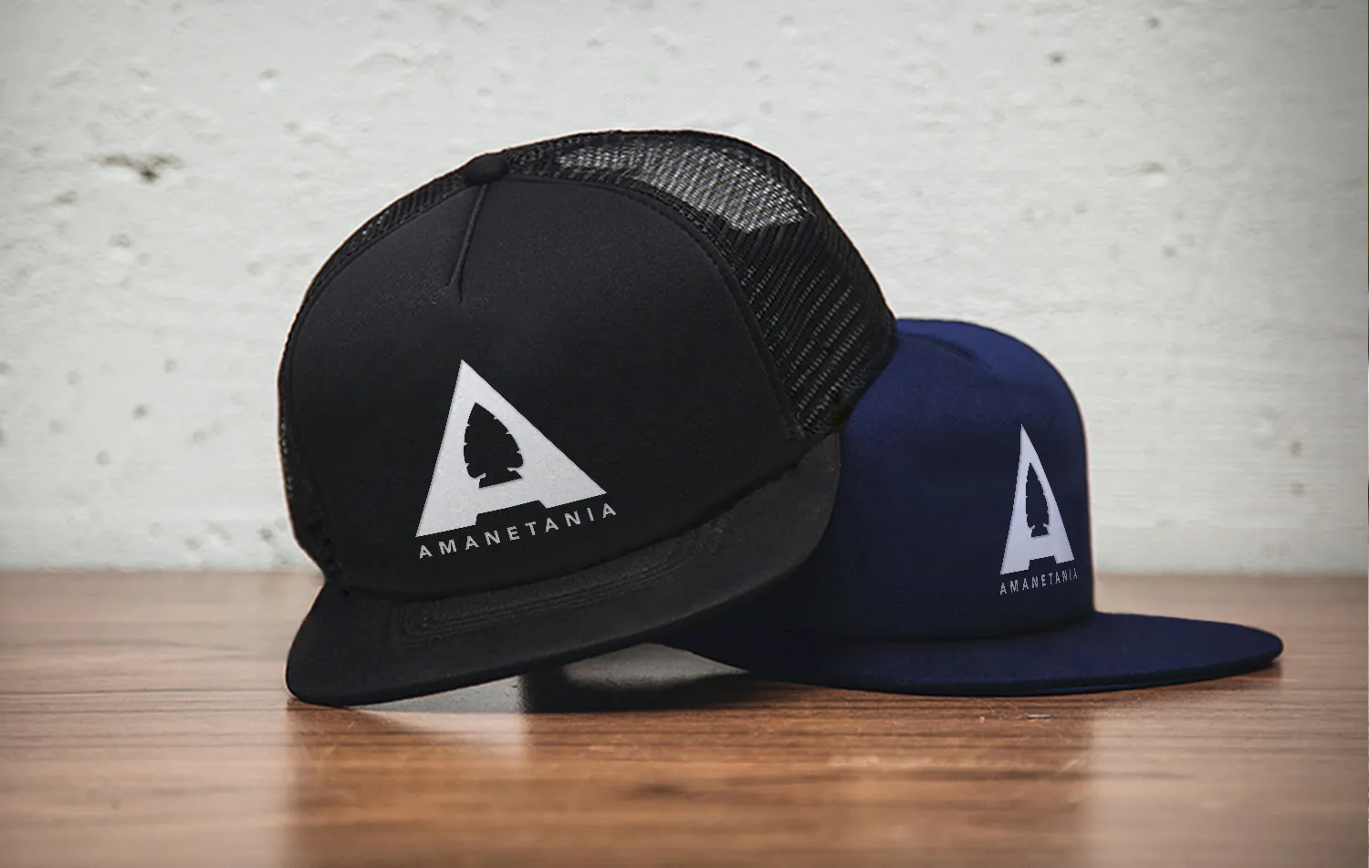 Two caps, one black and one navy, each carrying the Amanetania mark in white