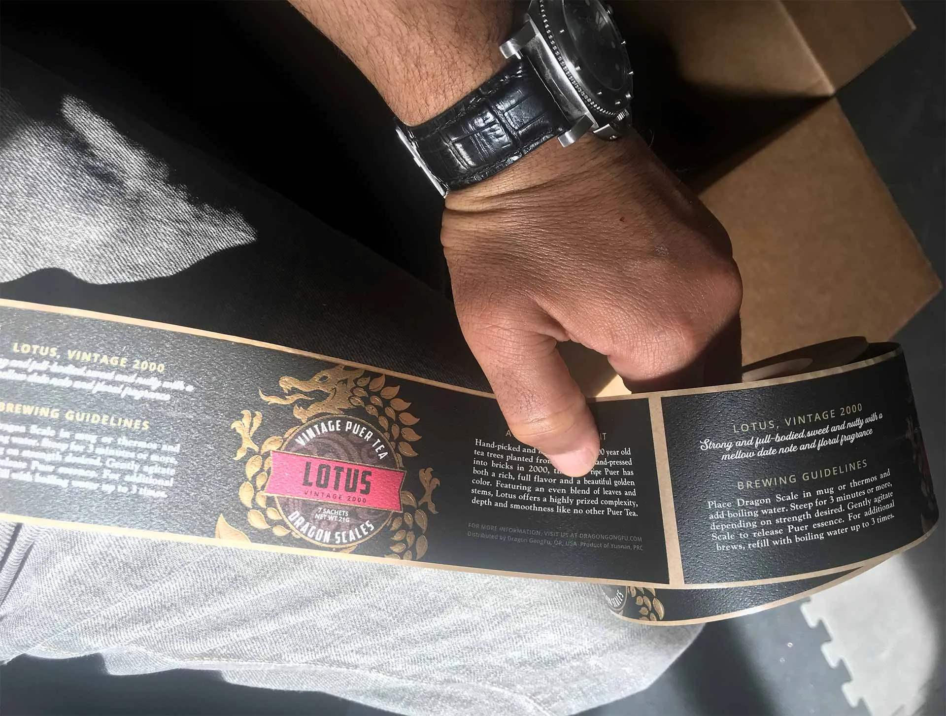 A printed Lotus label wrap held in hand against the tin it wraps, checked at production size