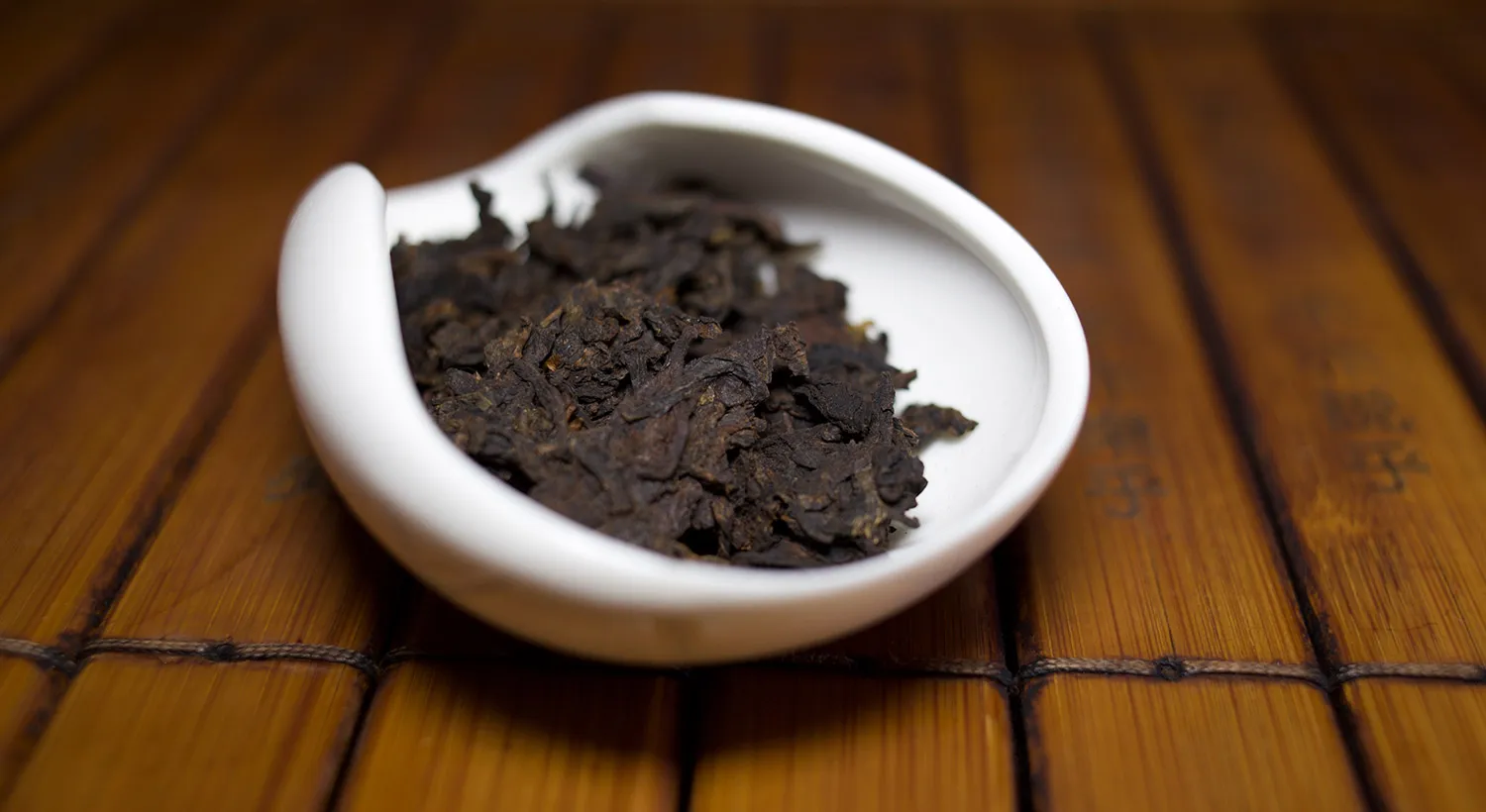 Aged Puer leaf in a white porcelain dish on a bamboo surface
