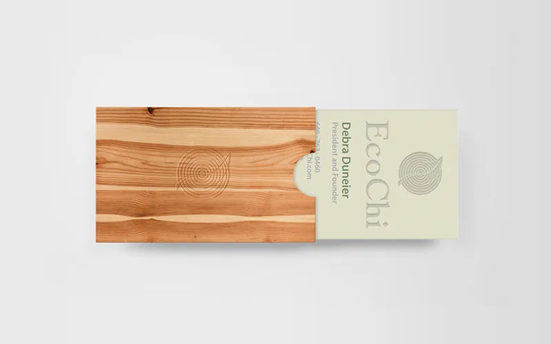 An EcoChi business card sliding out of a wooden sleeve engraved with the mark