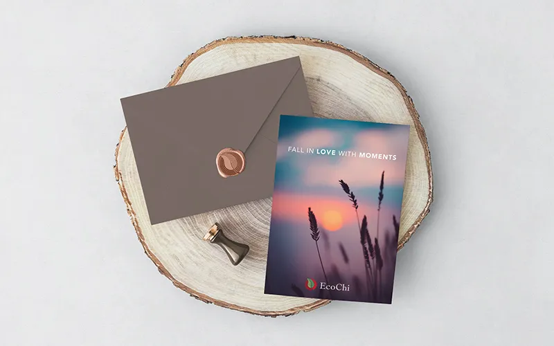 An EcoChi invitation card on a wood slice beside a wax-sealed envelope, printed with a dusk landscape and the mark