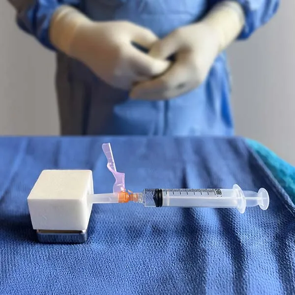 The HypoHolder on a blue surgical drape with a syringe secured in the foam, a gowned and gloved clinician working behind it