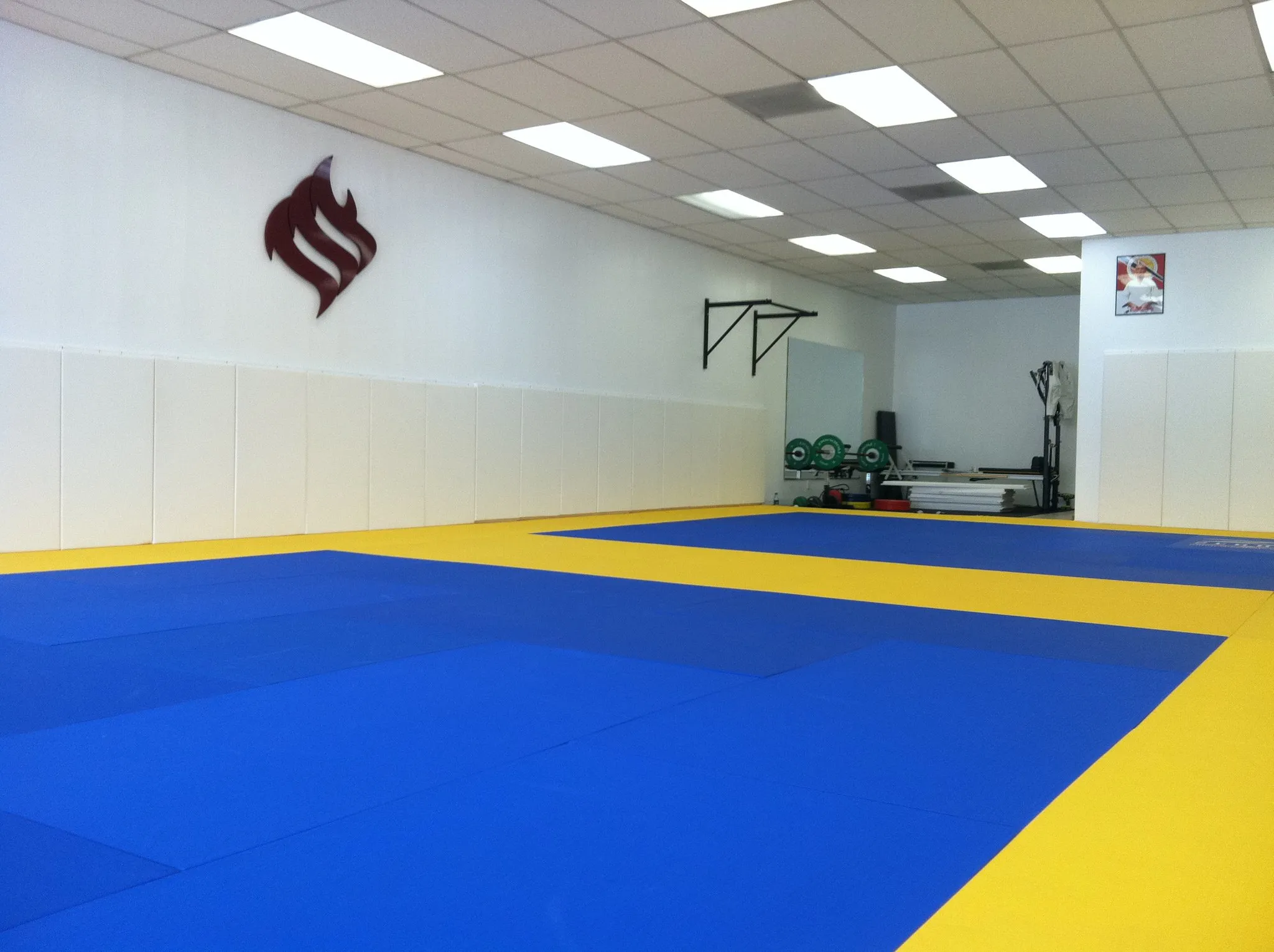 The empty Jiu Jitsu Foundation training room, blue and yellow mats with the mark on the far wall
