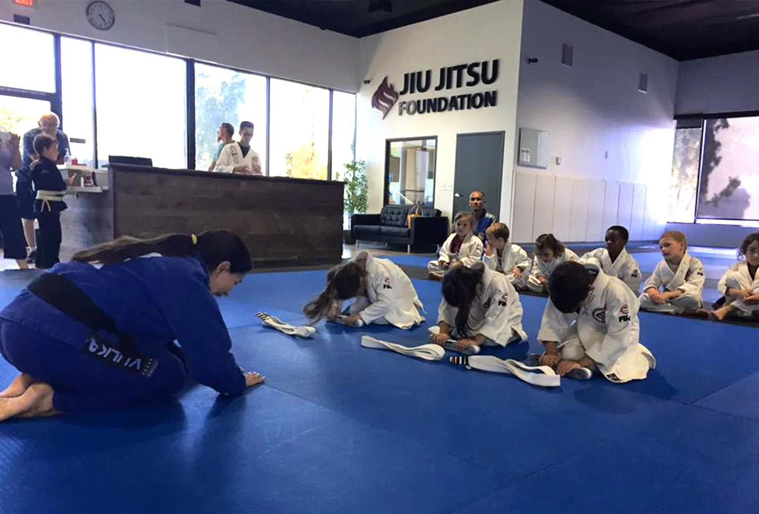A kids belt ceremony on the mats, the academy sign visible behind the group