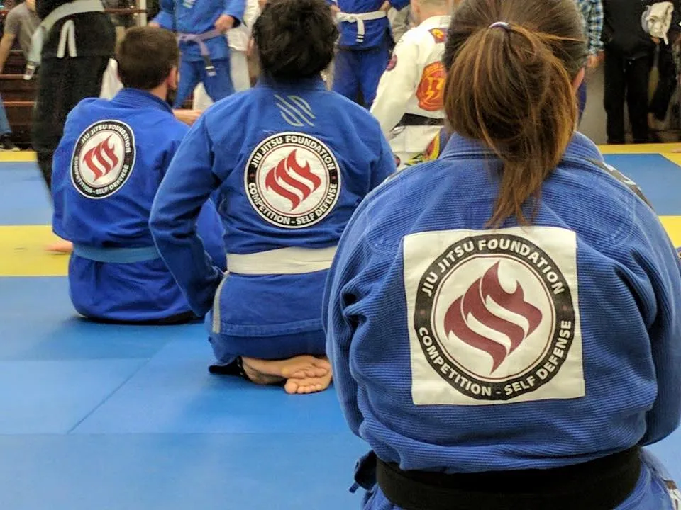 Members kneeling in blue gis, the academy back patch repeated across the row