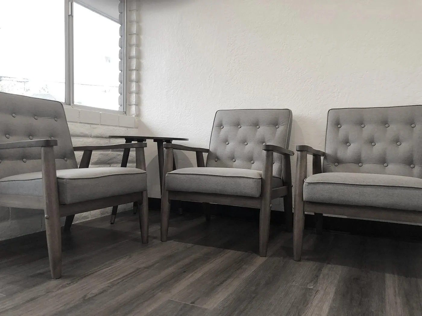 The waiting area: three grey mid-century chairs and a small table beside a window