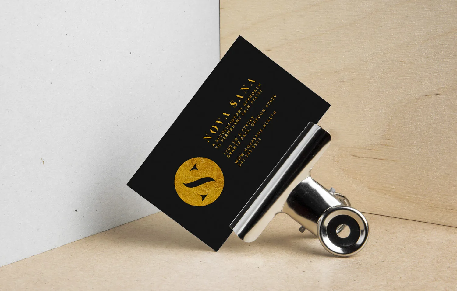 A business card in gold foil on black, propped against a clip