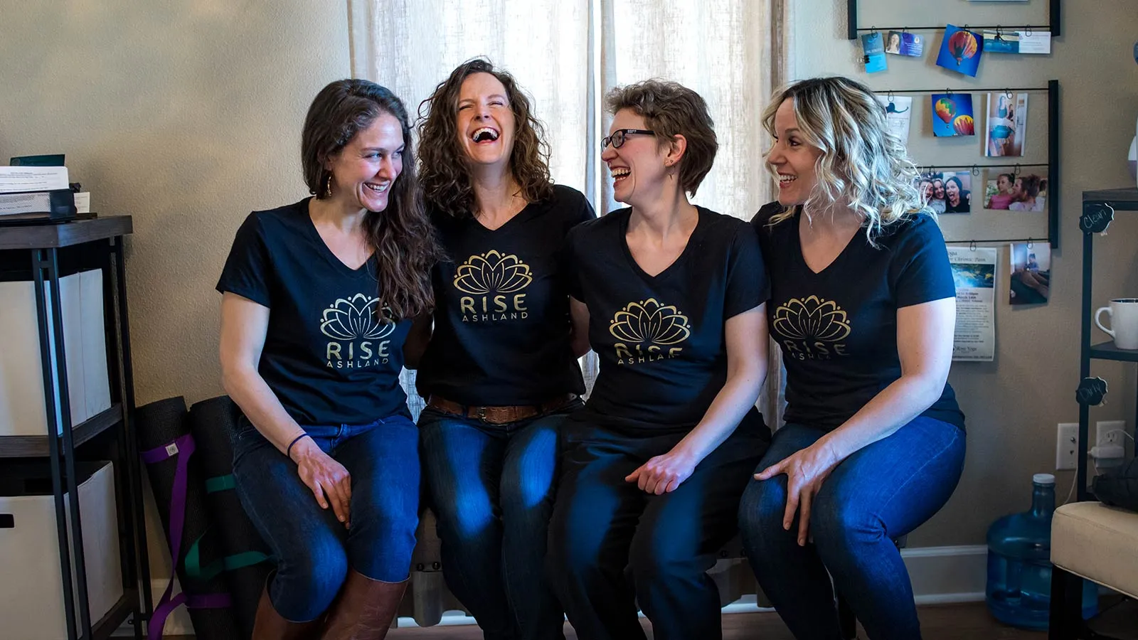 Four members of the Rise Ashland practice laughing together in the practice space, all wearing Rise Ashland branded shirts with the gold lotus mark