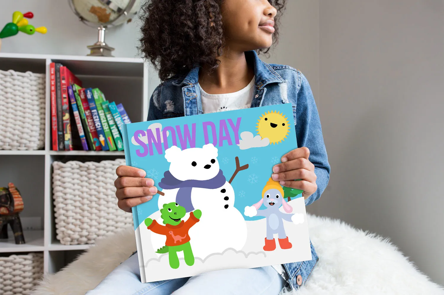 A child holding the Sputtens Snow Day picture book, the characters building a snowman on the cover