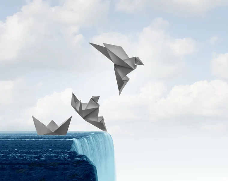 An origami paper boat at the edge of a waterfall transforming into a paper bird taking flight