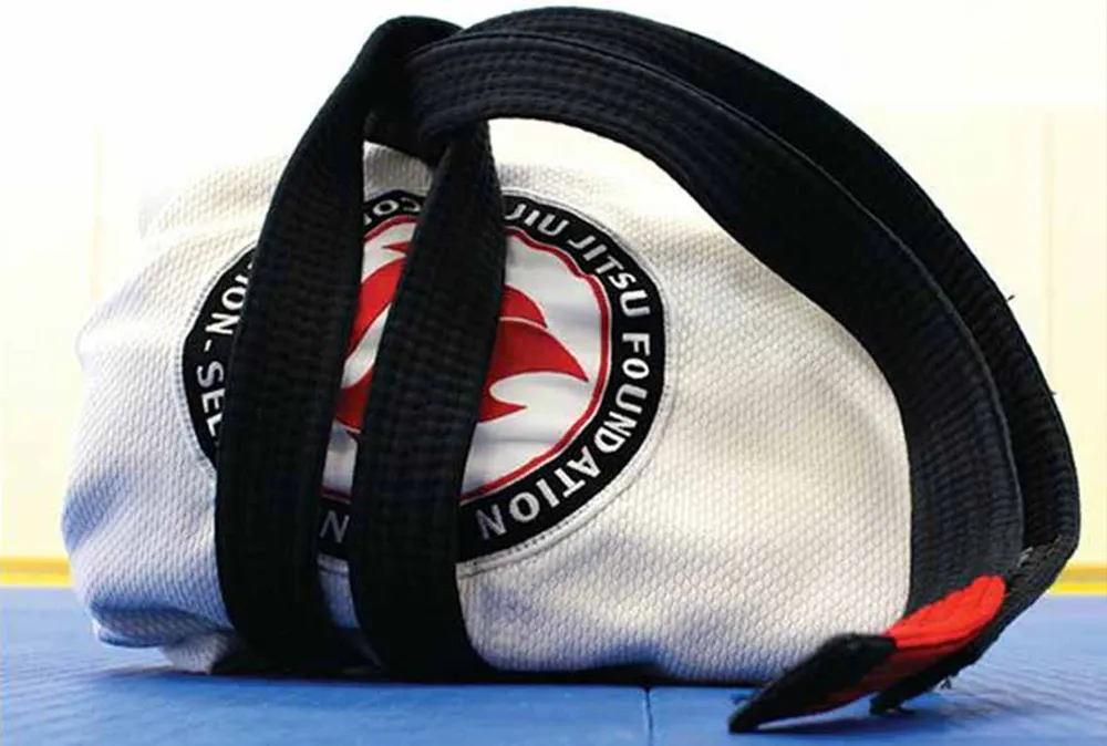 A folded white gi with the circular Jiu Jitsu Foundation patch, a black belt laid across it