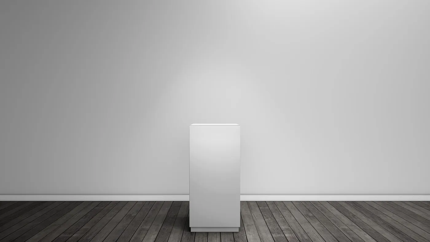 An empty white display pedestal on a dark wood floor against a lit gallery wall