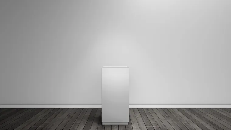 An empty white display pedestal on a dark wood floor against a lit gallery wall