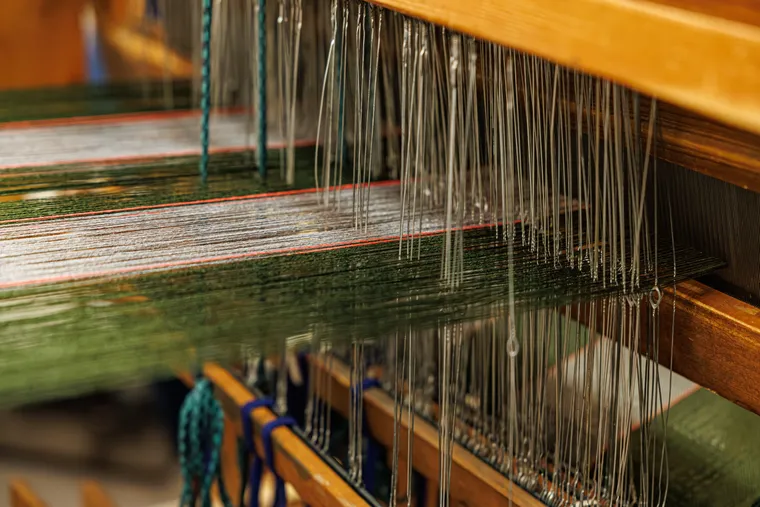 Close-up of a weaving loom with warp threads passing through rows of metal heddles