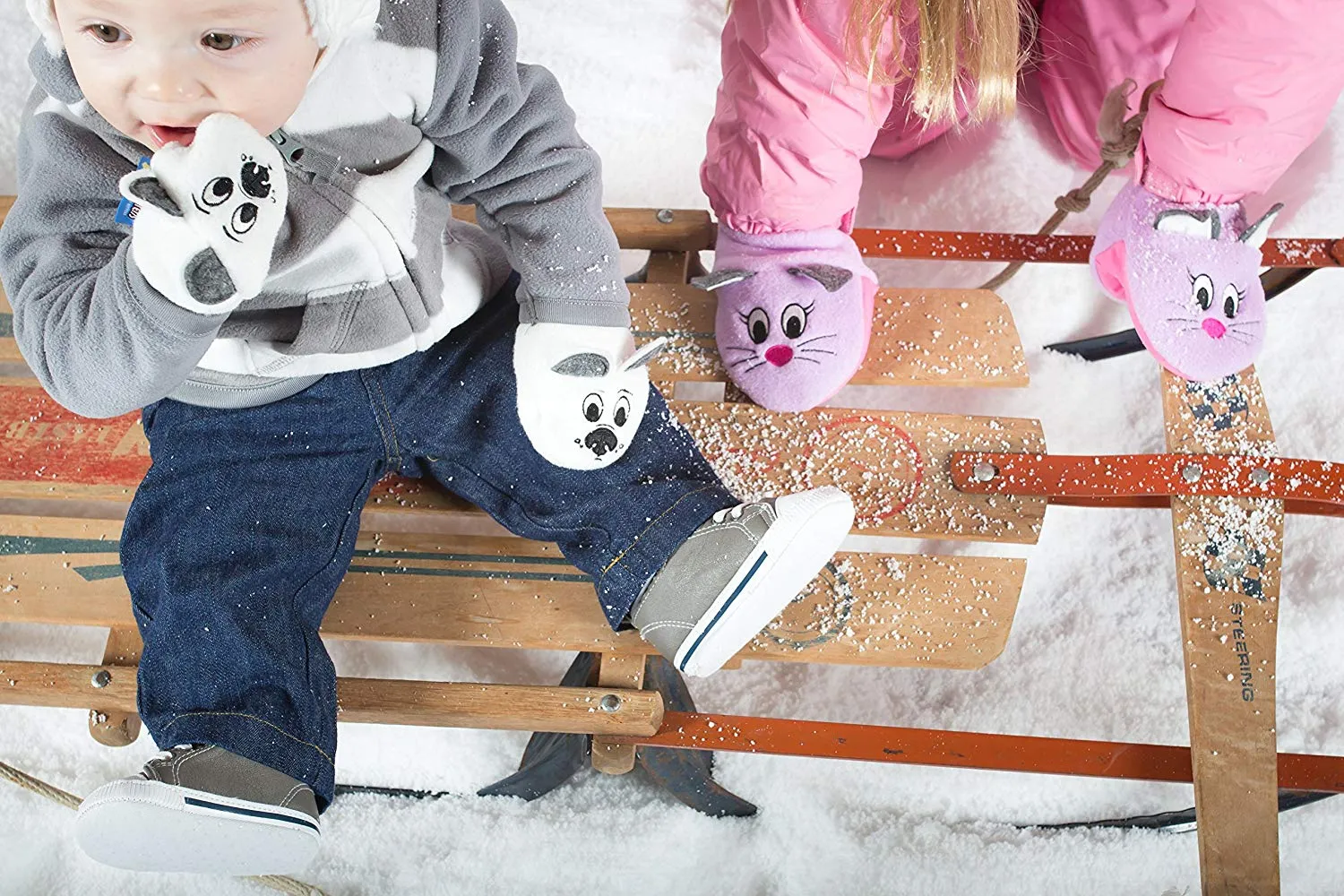 Two children on a sled in the snow, both wearing Sputtens character mittens